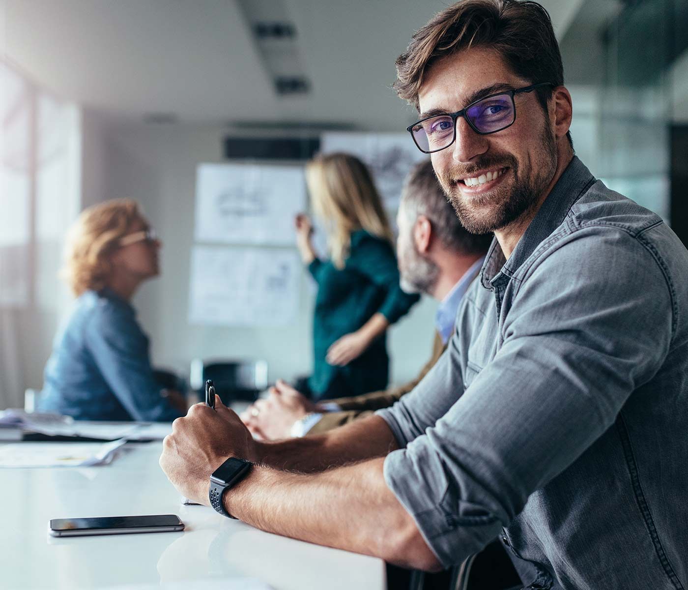 Un hombre sonríe a la cámara mientras está sentado en una reunión.